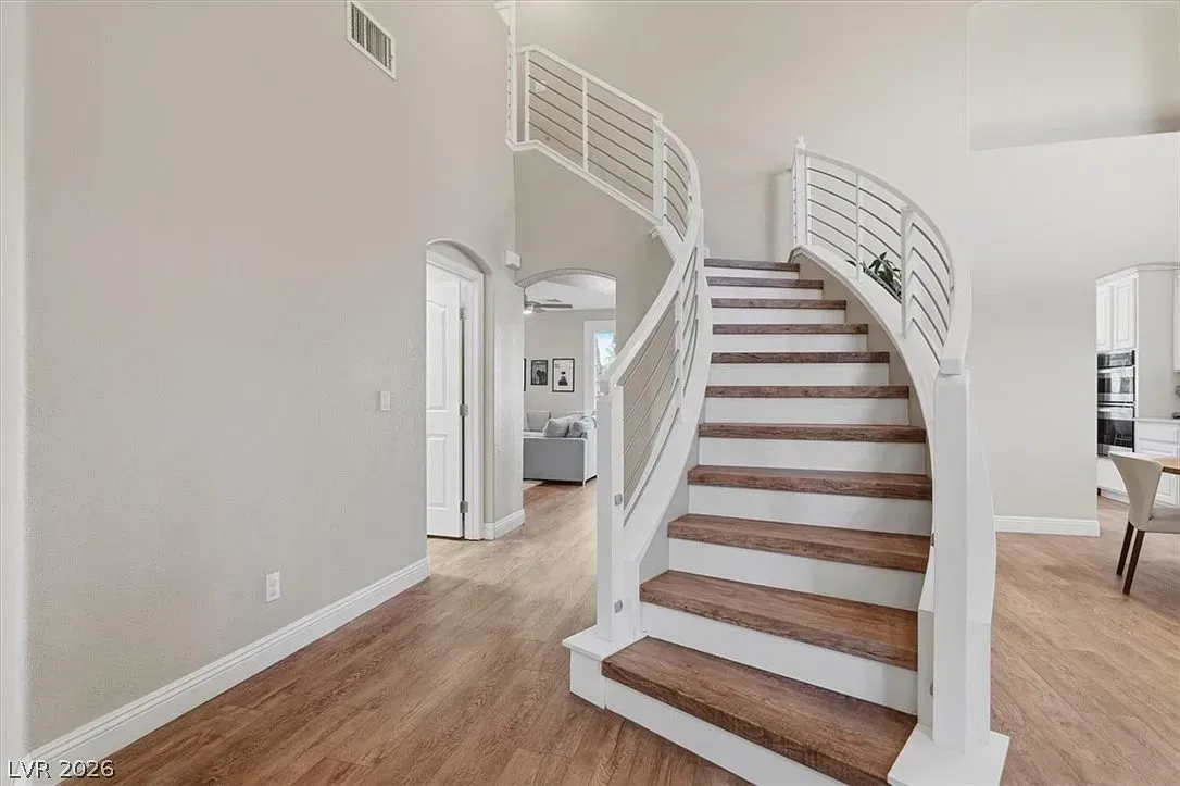 Bright foyer with curved white staircase, hardwood floors, and neutral walls leading to an upstairs landing