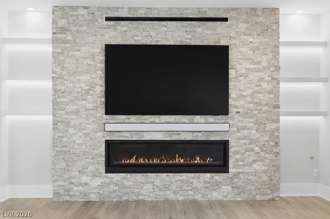 Modern living room wall with a large TV, linear fireplace, and stone accent surround flanked by white shelves