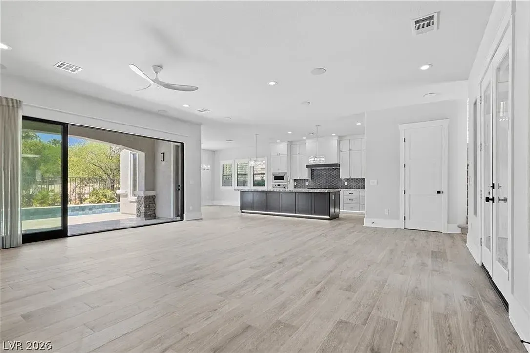 Bright open-concept living room with kitchen, light wood floors, white walls, and sliding glass doors to a patio