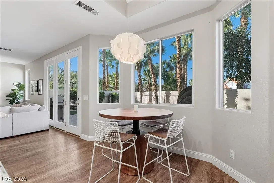 Bright dining nook with round table, white chairs, wood floor, and large windows overlooking trees.