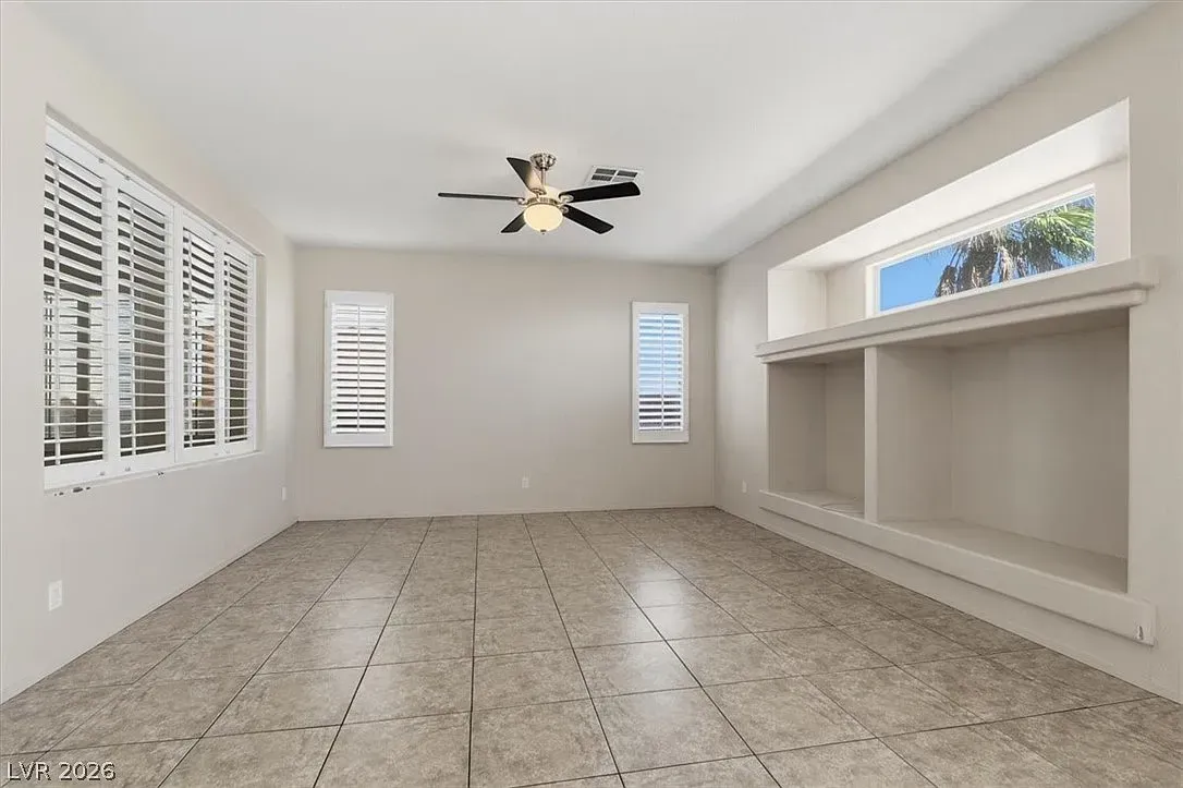 Empty bright living room with tile floor, white walls, ceiling fan, windows, and a built-in wall niche