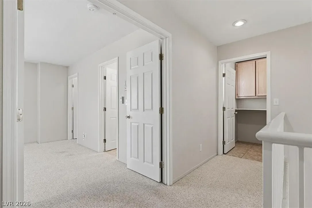 Bright upstairs hallway with white doors, carpet, and a view into a small closet or bathroom.