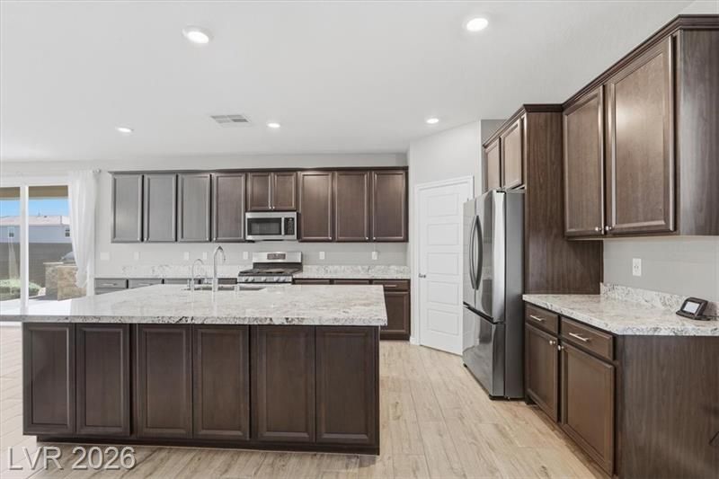 Modern kitchen with dark wood cabinets, white countertops, stainless steel appliances, and light wood floors