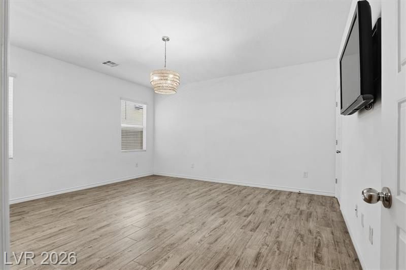 Empty white bedroom with wood flooring, ceiling light, window, and wall-mounted TV