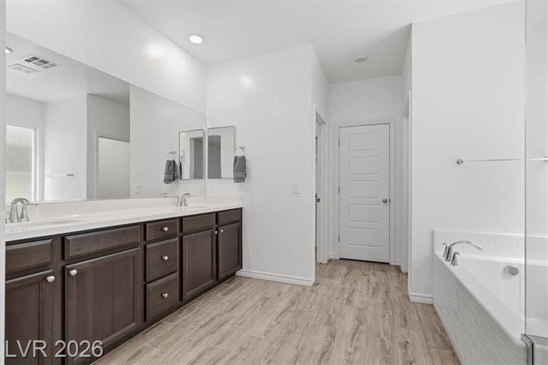Bright modern bathroom with double vanity, white tub, and light wood flooring