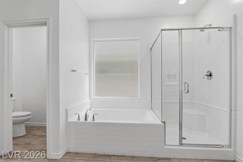 Bright white bathroom with soaking tub, window, and glass-enclosed shower beside a toilet.