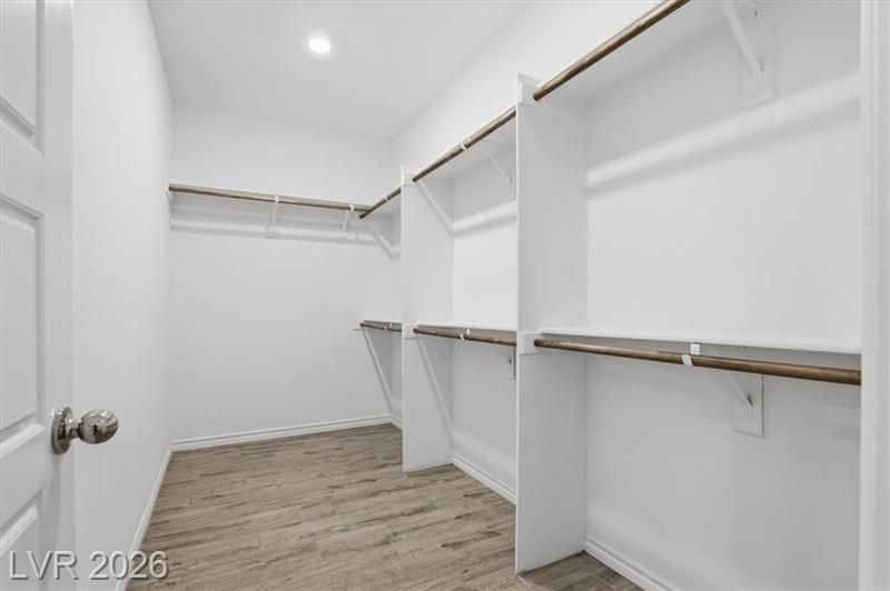 Spacious walk-in closet with white shelving and hanging rods, gray wood-look flooring, and a sloped ceiling.