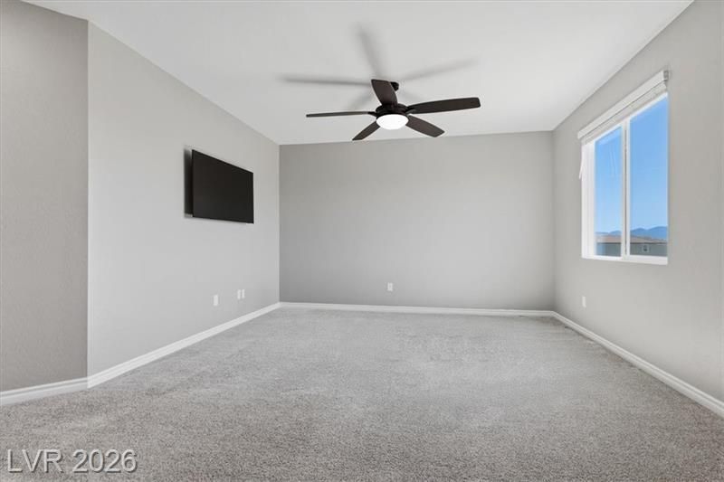 Empty gray bedroom with carpet, ceiling fan, wall-mounted TV, and two windows with mountain views