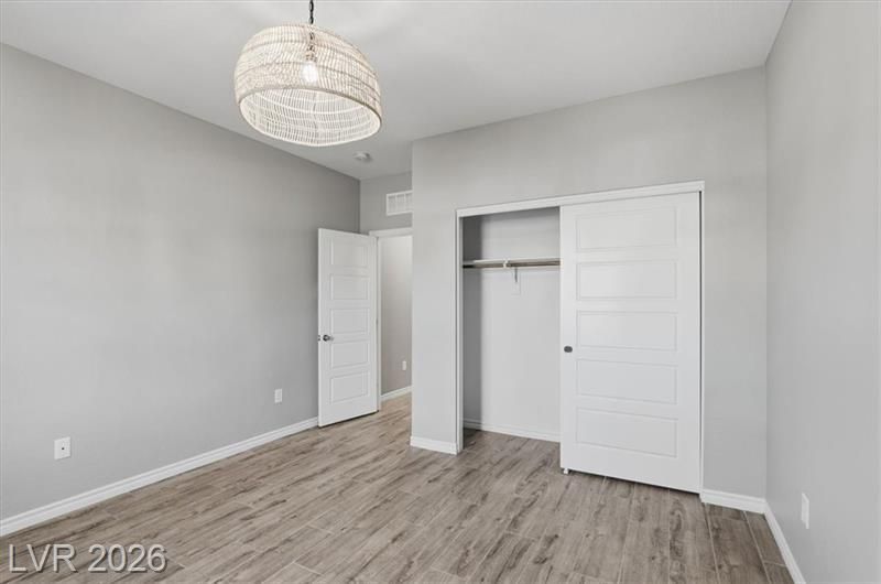 Empty gray bedroom with wood-look flooring, ceiling light, open closet, and white door