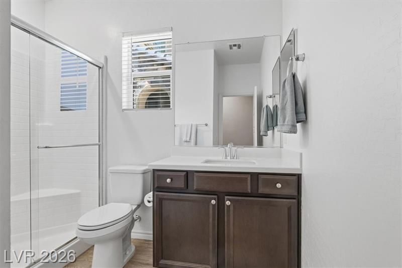 Small bathroom with toilet, glass shower, dark vanity, mirror, and white walls.