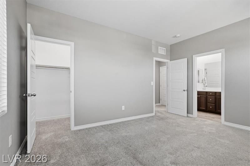 Empty bedroom with gray walls, carpeted floor, open closet, and bathroom visible through doorway.