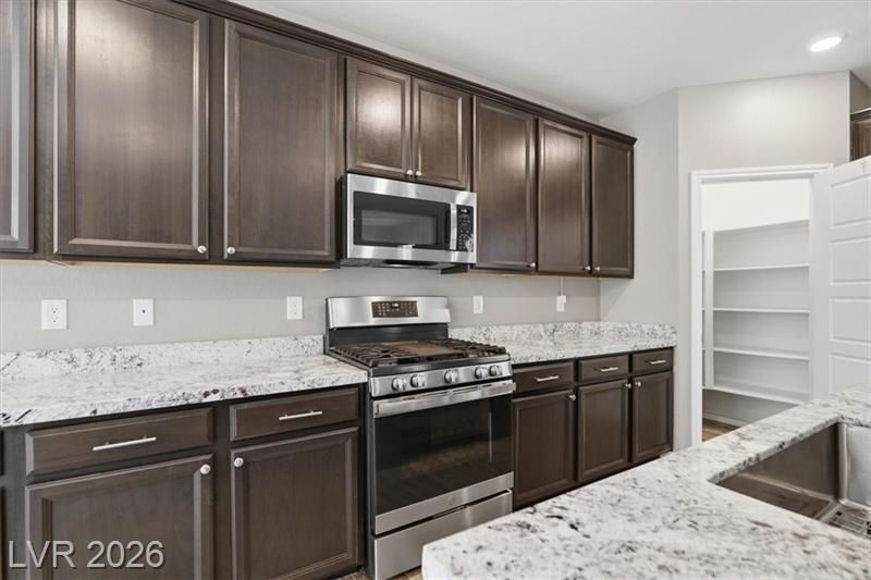 Modern kitchen with dark wood cabinets, stainless steel appliances, and white marble countertops