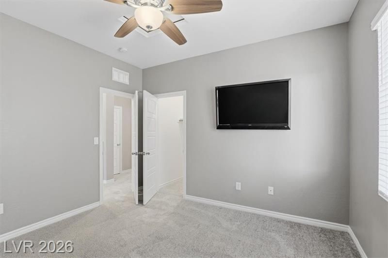 Empty gray bedroom with ceiling fan, wall-mounted TV, open door, and carpeted floor.