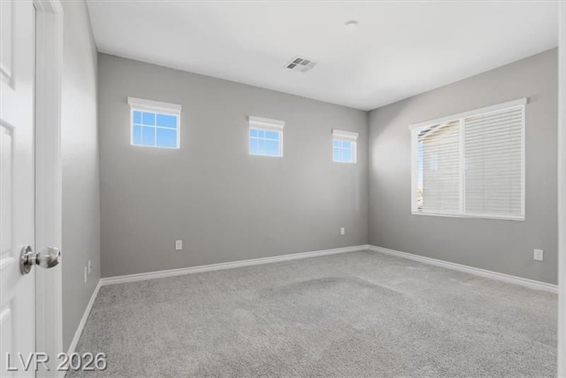 Empty light gray bedroom with carpet, white trim, small high windows, and a larger window with blinds.