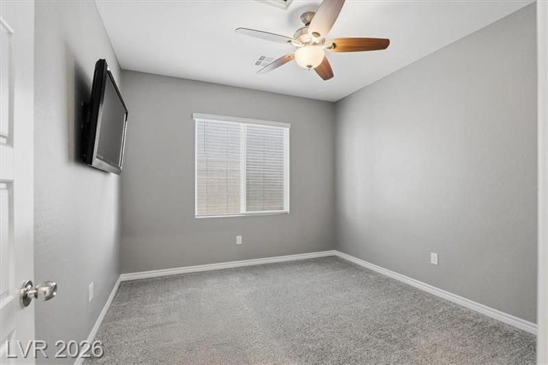 Empty gray bedroom with carpet, ceiling fan, wall-mounted TV, and a window with blinds