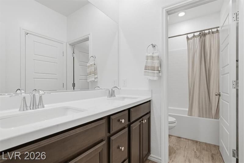 Bright bathroom with double vanity, large mirror, and shower with beige curtain.