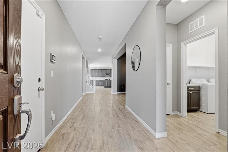 Bright hallway in a modern home with light wood floors, gray walls, and a bathroom doorway on the right.