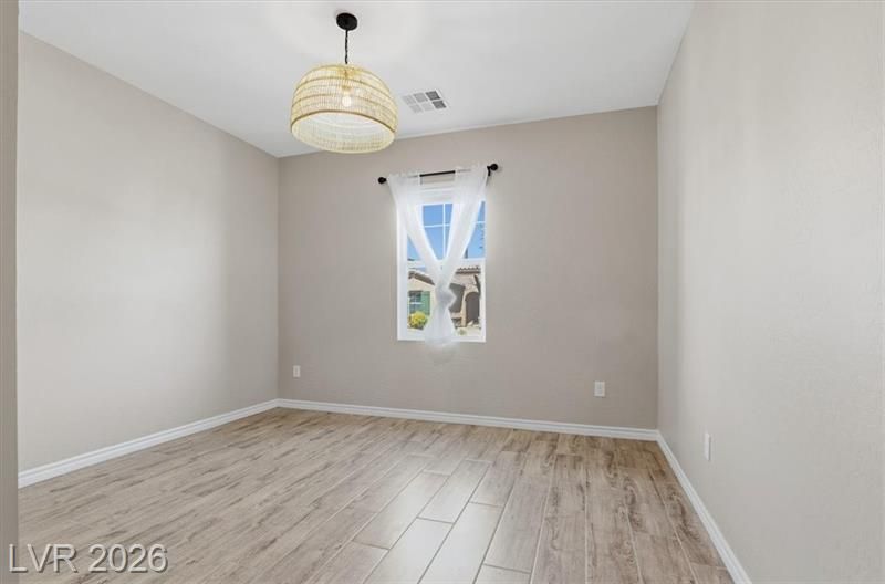 Empty light-gray bedroom with wood-look floors, hanging light fixture, and a small window.