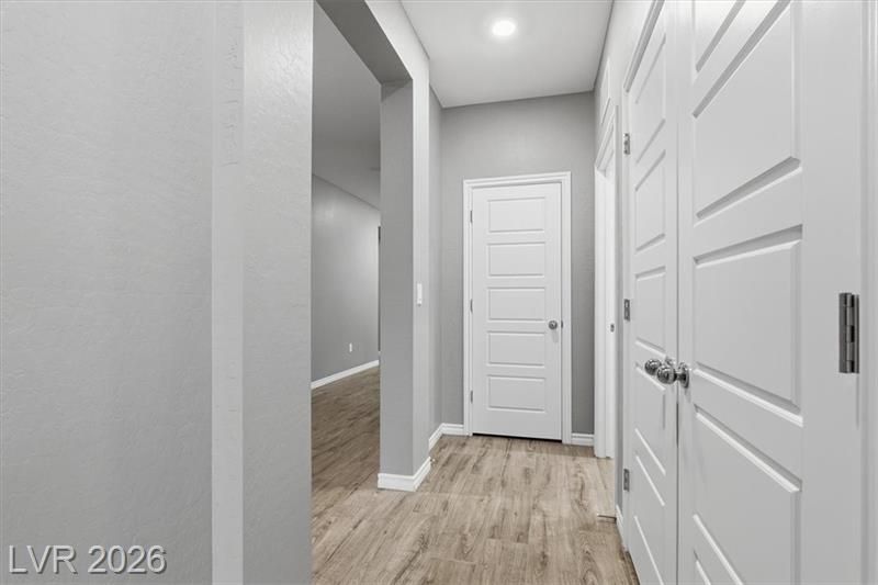 Bright gray hallway with white doors, wood-look floors, and recessed ceiling lights.