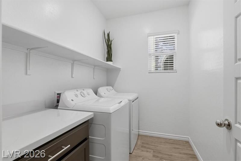 White laundry room with stacked washer and dryer, countertop, shelves, and a small window.