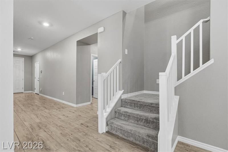 Gray hallway with light wood floors and carpeted stairs leading up