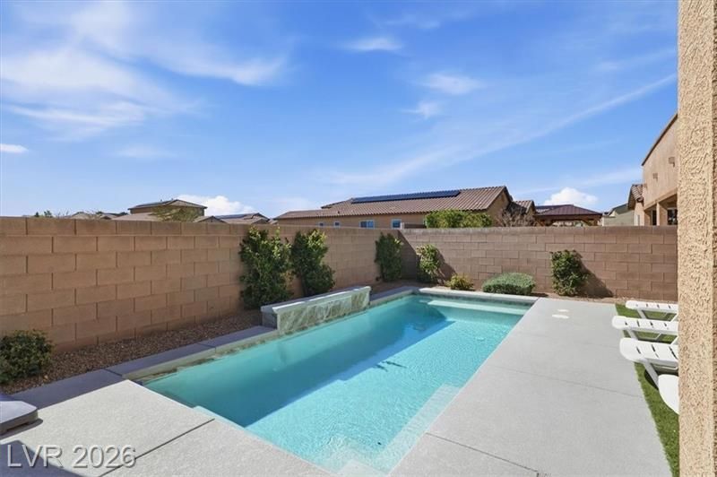 Backyard swimming pool with turquoise water, tan block walls, and lounge chairs under a sunny blue sky