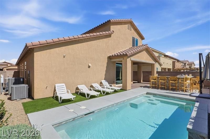 Backyard patio with a swimming pool, lounge chairs, and a shaded dining area beside a stucco house