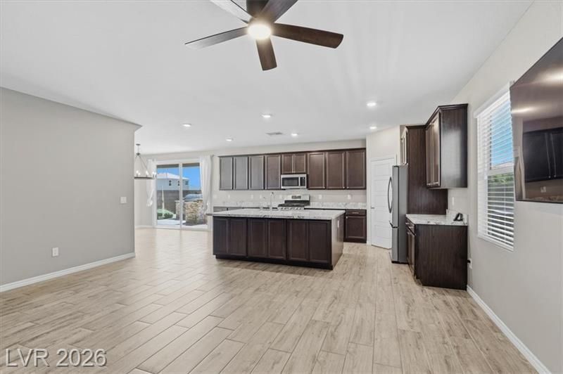 Bright modern kitchen and living area with light wood floors, dark cabinets, island, and ceiling fan