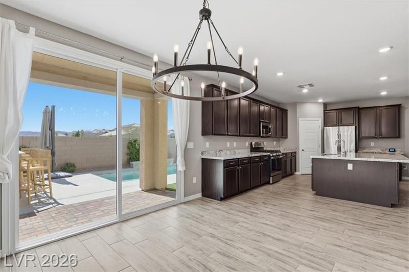Modern kitchen with dark cabinets, island, chandelier, and sliding glass doors to a patio and pool.