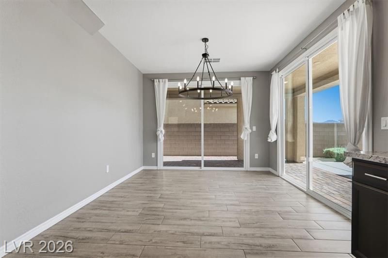 Empty dining area with light wood floors, gray walls, chandelier, and sliding glass doors.