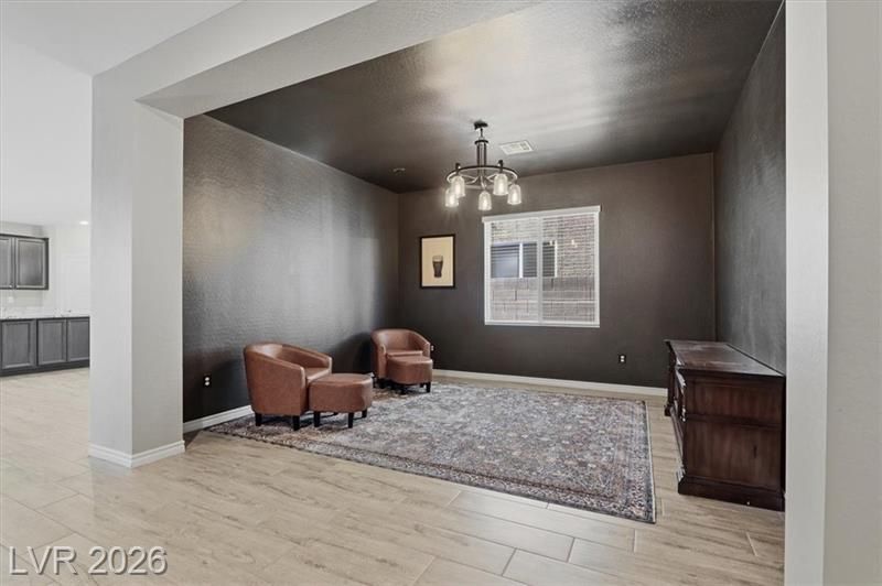 Modern living room with dark walls, two brown chairs, chandelier, window, and patterned rug
