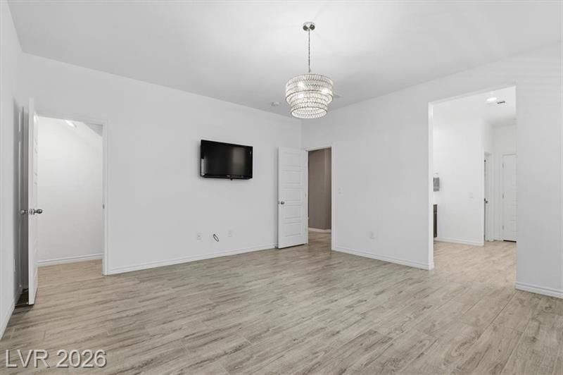 Empty white living room with light wood floors, wall-mounted TV, and modern ceiling light