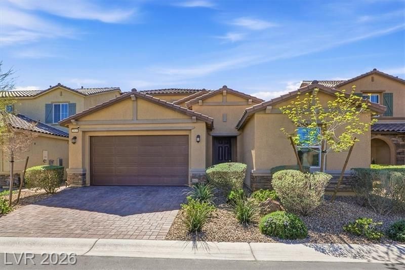 Single-story suburban house with tan stucco, brown garage door, and a small front desert garden