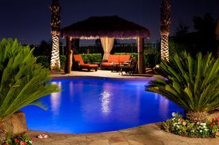 Nighttime resort pool with blue water, lit cabana, and palm trees along the deck