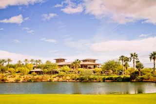 Lakefront resort with palm trees, modern houses, and blue sky reflected in calm water
