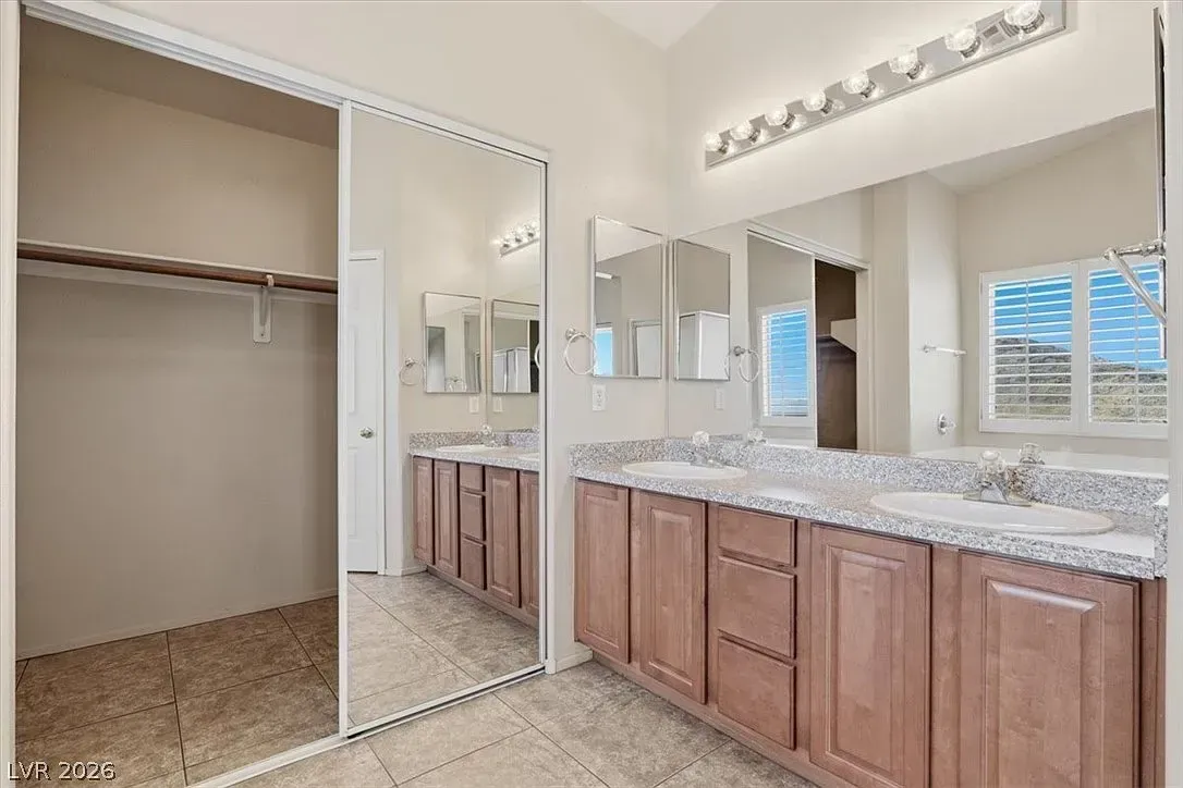 Spacious bathroom with double vanity, large mirror, tiled floor, and open walk-in closet.