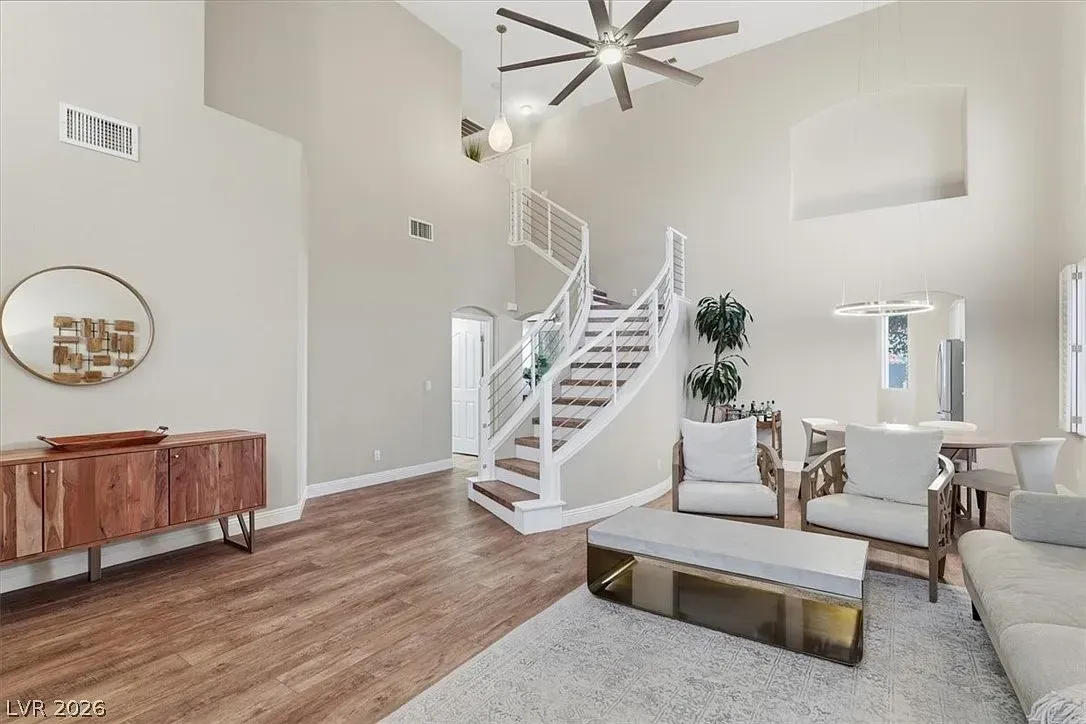 Bright modern living room with white staircase, wood floors, gray sofa, and large ceiling fan