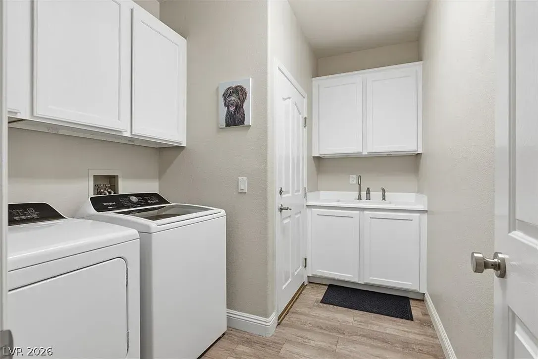 Laundry room with white washer and dryer beside a small sink and cabinets, light walls, and wood floor