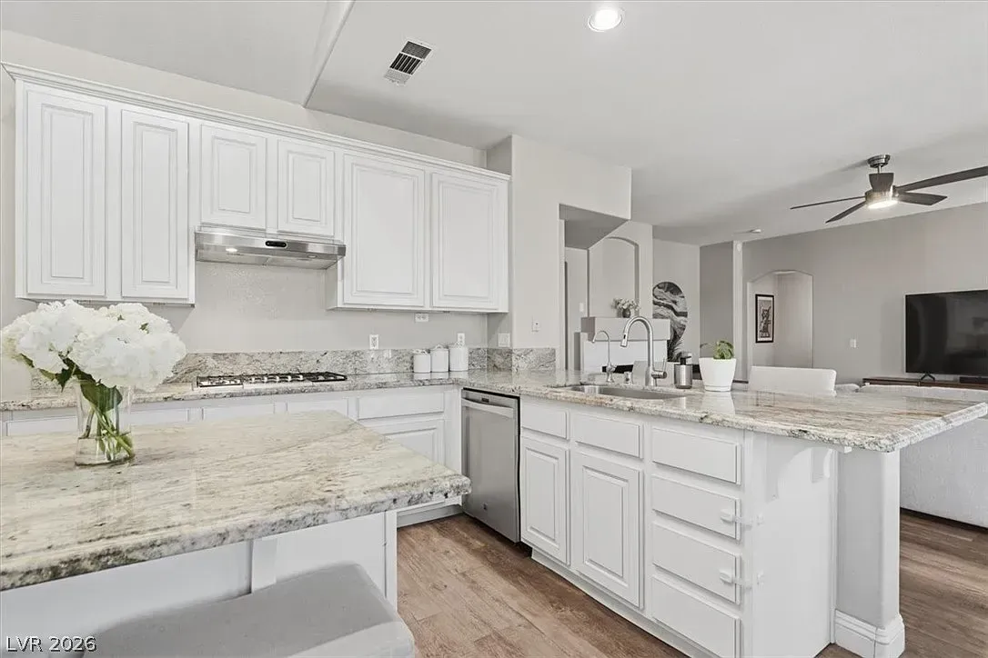Bright white kitchen with granite countertops, white cabinets, and stainless steel appliances