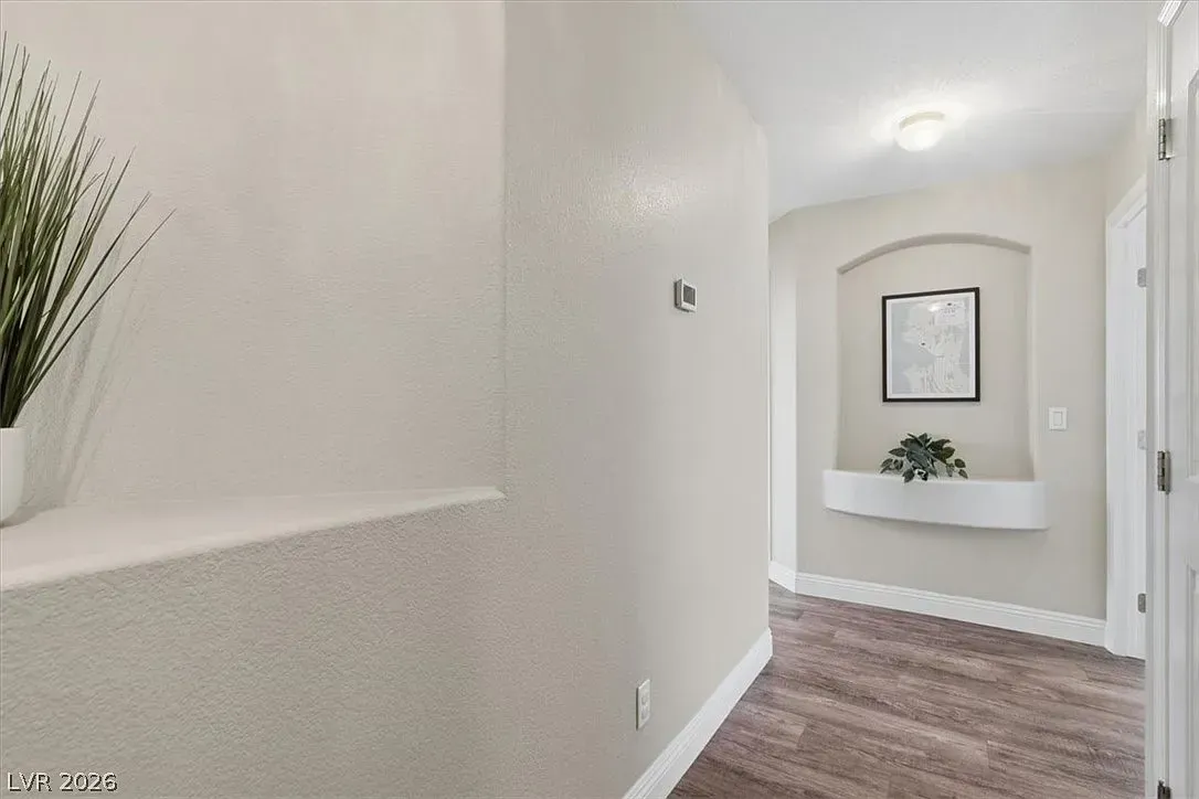 Bright hallway with white walls, wood flooring, and a small alcove with framed art and a plant display.