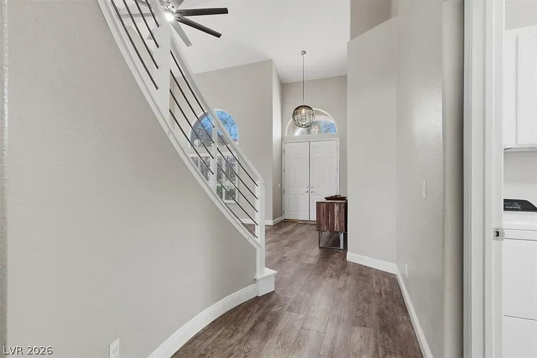Bright hallway with staircase, wood floors, ceiling fans, and a doorway at the end