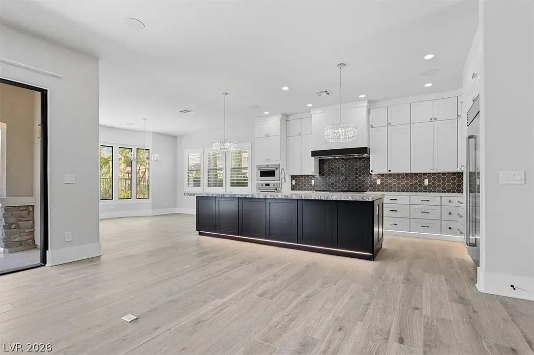 Bright modern kitchen with white cabinets, dark island, and large windows over light wood floors