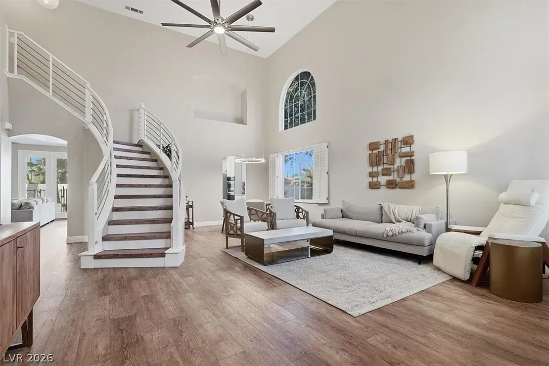 Bright living room with curved staircase, white walls, wood floors, and modern seating under a ceiling fan.