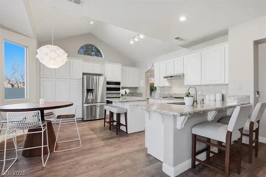 Bright white kitchen and dining area with stainless steel appliances, island seating, and wood floors