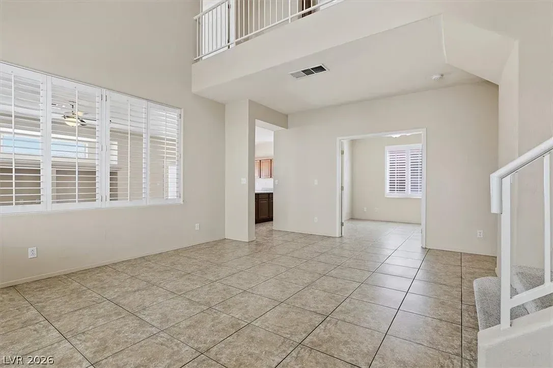 Bright empty living room with tile floor, white walls, large windows, and staircase railing