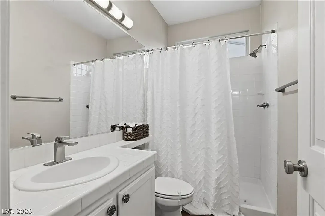 White bathroom with sink, toilet, shower curtain, and towel racks