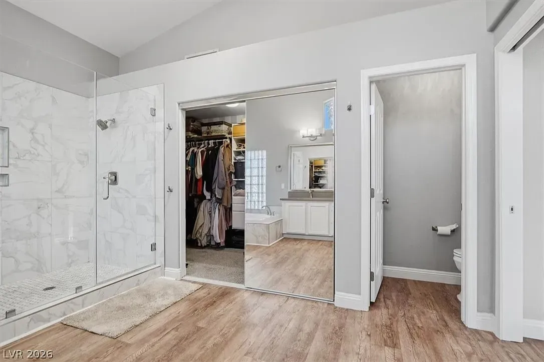 Bright bedroom with open closet, mirrored doors, marble shower, and small adjoining bathroom.