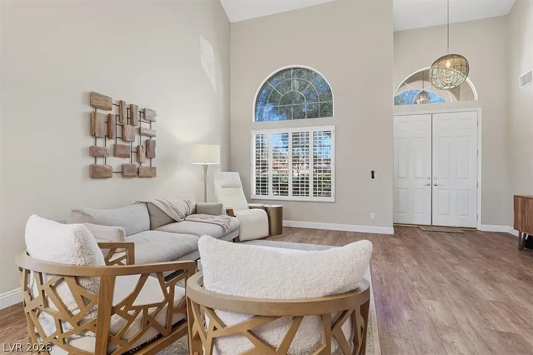 Bright living room with white sofa, two chairs, arched window, and double front doors