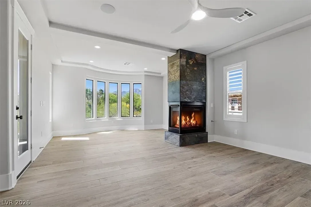 Bright empty living room with white walls, light wood floors, and a central modern fireplace.