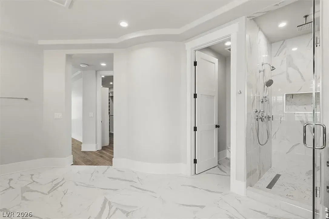 Bright white marble bathroom with glass shower, vanity, and doorway to a hallway